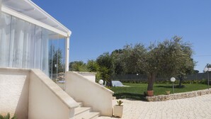 A modern building with a glass facade, a stone staircase leading to a covered entrance, and a paved courtyard with potted plants. - Apulian Villa (Conversano)