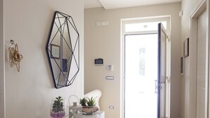 A modern hallway with a white console table, a geometric mirror, and a door leading to a bright room. - Apulian Villa (Conversano)