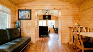 L’intérieur chaleureux d’un chalet avec un plancher en bois, un canapé en cuir, une table à manger avec des chaises, un ventilateur de plafond et un tableau accroché au mur.