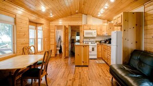 Un chalet confortable aux murs et au plancher en bois, avec un coin repas doté de chaises, une cuisine équipée et un canapé en cuir.
