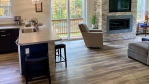 A modern kitchen with a stone accent wall, a large TV mounted above a fireplace, and a bar area with stools.
