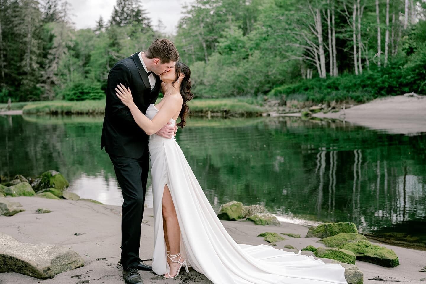 A couple embracing by a lake with a forest in the background.