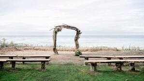 A rustic wooden archway with floral decorations, leading to a beachside setting with benches on either side. - Beachfront House- The Sea Eagle (Sekiu)