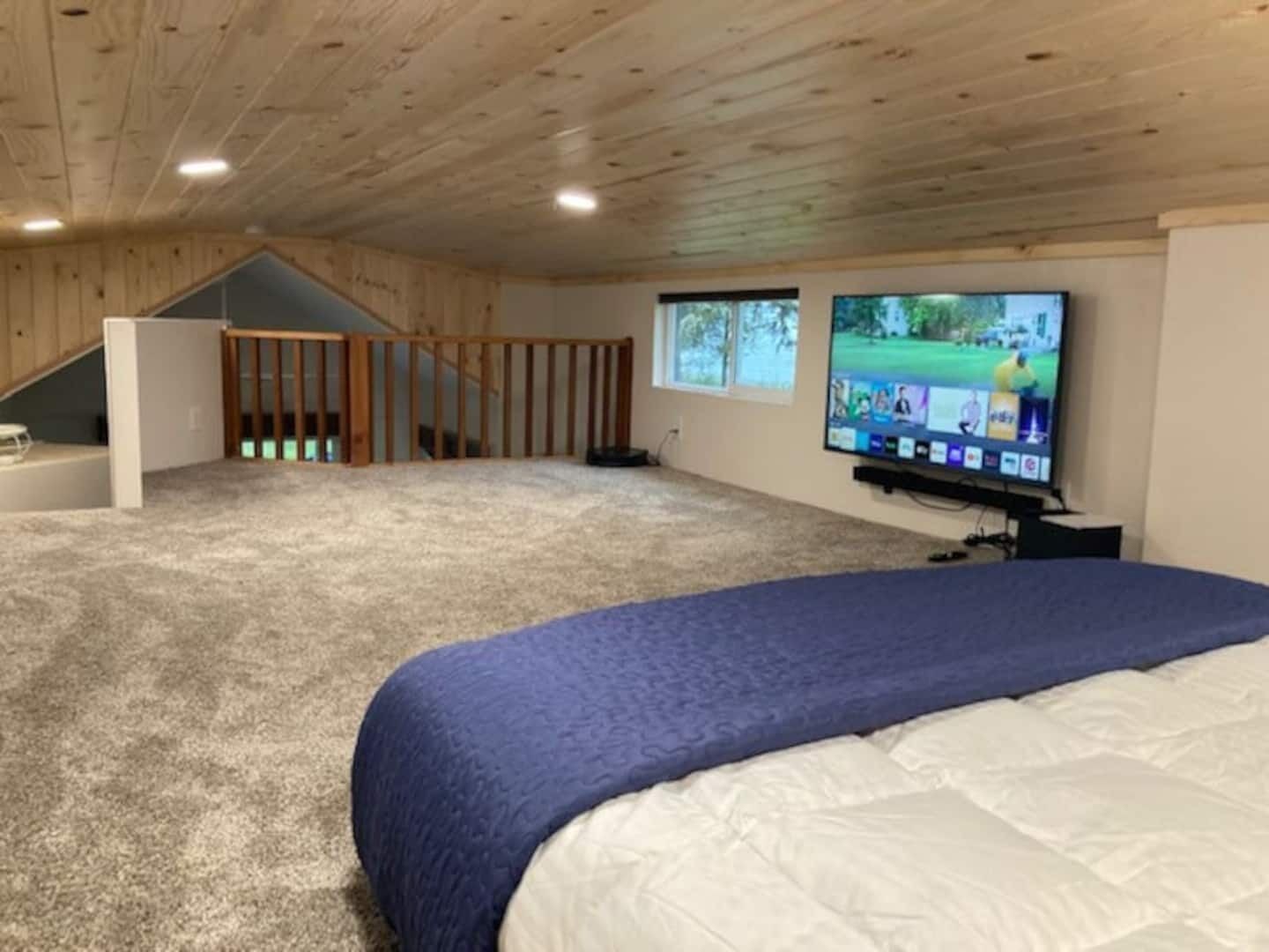 A spacious room with a large bed, a television mounted on the wall, and a view of the outdoors through a window.