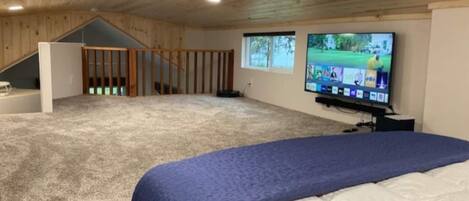 A spacious room with a large bed, a television mounted on the wall, and a view of the outdoors through a window.