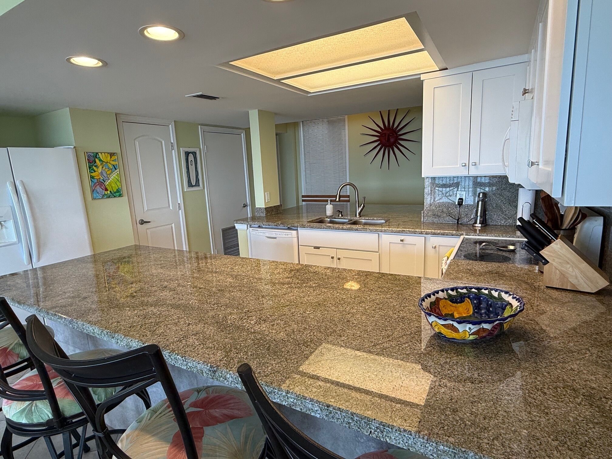 A kitchen with a granite countertop, white cabinets, a built-in dishwasher, and a decorative bowl on the island.