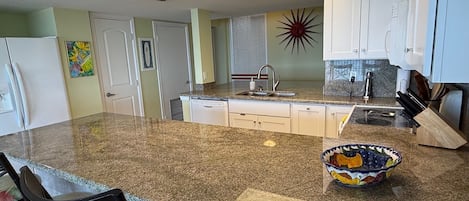 A kitchen with a granite countertop, white cabinets, a built-in dishwasher, and a decorative bowl on the island.
