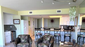 A spacious living area with a sofa, two armchairs, and a coffee table. There is a kitchen area with a refrigerator, sink, and bar stools. - Fabulous 5th floor beachfront; fully appointed; discount for weekdays & 7 nights (South Padre Island)