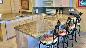 A kitchen with a granite countertop, white cabinets, a stainless steel sink, a microwave, a stove, and bar stools. - Fabulous 5th floor beachfront; fully appointed; discount for weekdays & 7 nights (South Padre Island)