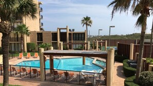 A swimming pool with lounge chairs, surrounded by palm trees and a building with balconies. - Fabulous 5th floor beachfront; fully appointed; discount for weekdays & 7 nights (South Padre Island)
