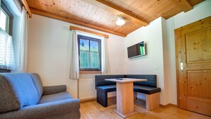 Une pièce chaleureuse avec un plafond en bois, un canapé, une petite table et un téléviseur fixé au mur.