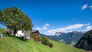 Une maison blanche avec une clôture en bois et un grand arbre sur une colline verdoyante.
