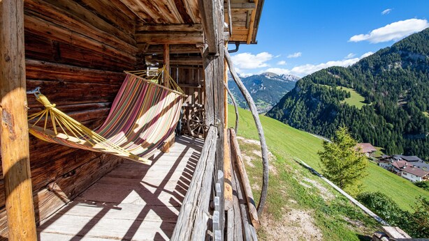 Une cabane en bois avec un hamac sur le porche, donnant sur un paysage montagneux.