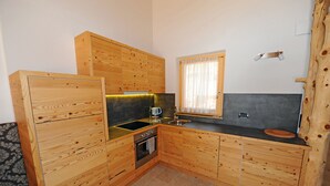Une cuisine compacte avec des meubles en bois, un four encastré et une fenêtre ornée de rideaux légers.