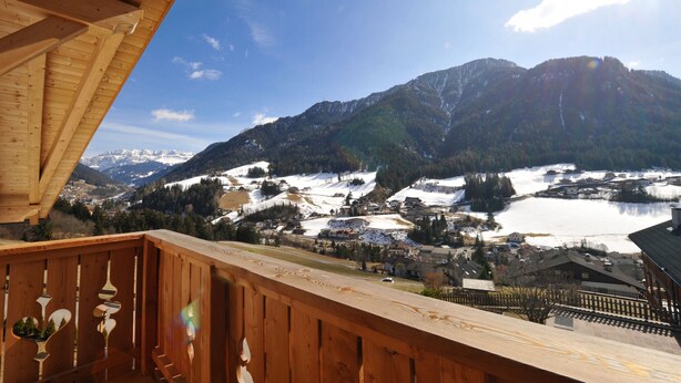 Un balcon en bois donnant sur un paysage montagneux, avec un lac, des bâtiments et des collines enneigées.