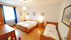 A hotel room with a wooden bed, a wooden desk, a chair, a bedside table with a lamp, and a window with curtains. - Apartments Valverda 111A (Ortisei)