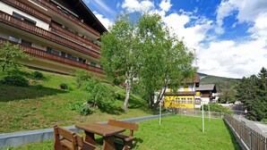 A grassy area with a wooden bench and picnic table, a yellow building, and a multi-story building with balconies. - Apartments Valverda 111A (Ortisei)