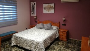 Un dormitorio con cama, mesitas de noche, un banco y obras de arte en las paredes.