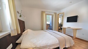 Quarto com cama, televisão na parede e janela com cortinas.