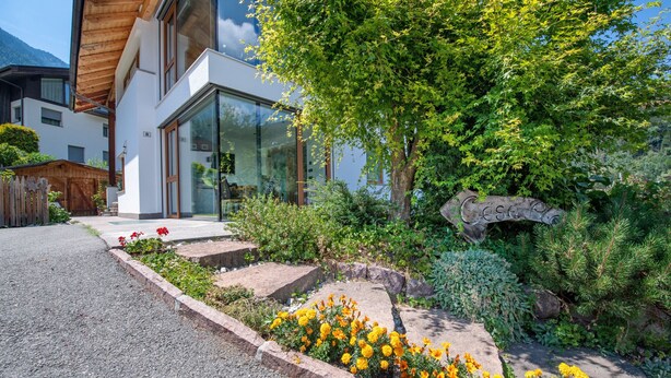 Ett modernt hus med en välskött trädgård, som innehåller en mängd olika växter och blommor.