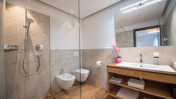 A modern bathroom with a glass-enclosed shower, a bidet, a toilet, and a wooden vanity with a sink and towel racks.