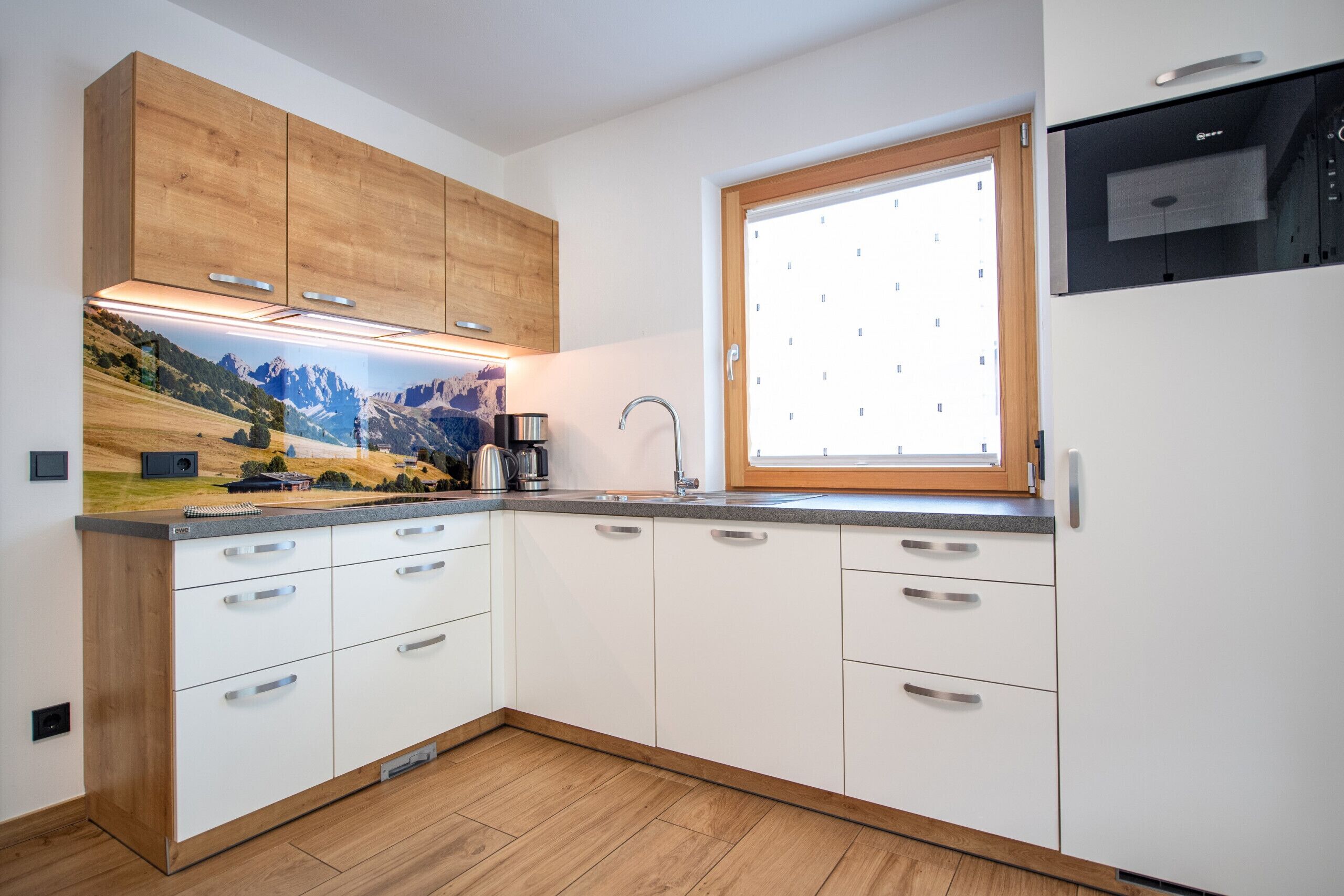 Une cuisine moderne avec des armoires blanches, un plan de travail en bois, une cuisinière intégrée et une fenêtre donnant sur les montagnes.