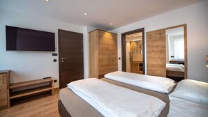Una camera d'albergo moderna con due letti, una televisione, un'armadio in legno e uno specchio.