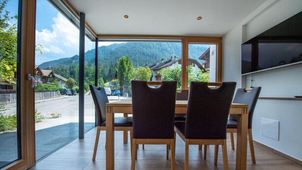Zona pranzo con un'ampia finestra, tavolo e sedie in legno.