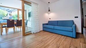 Un soggiorno moderno con un divano blu, pavimento in legno e una porta vetrata che dà su un balcone.
