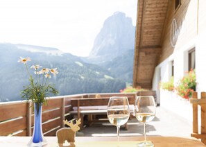Une table avec deux verres à vin et un vase de fleurs, le tout placé sur un balcon donnant sur les montagnes.