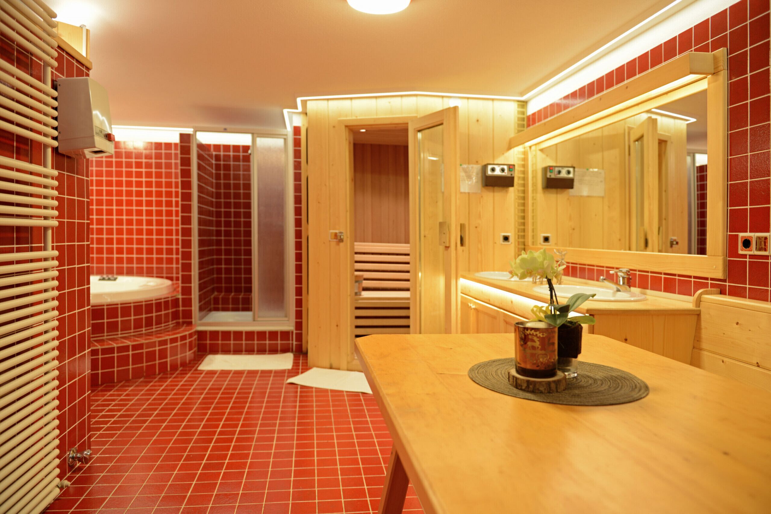 A bathroom with red tiles, a wooden vanity, a sink, a mirror, and a shower enclosure.