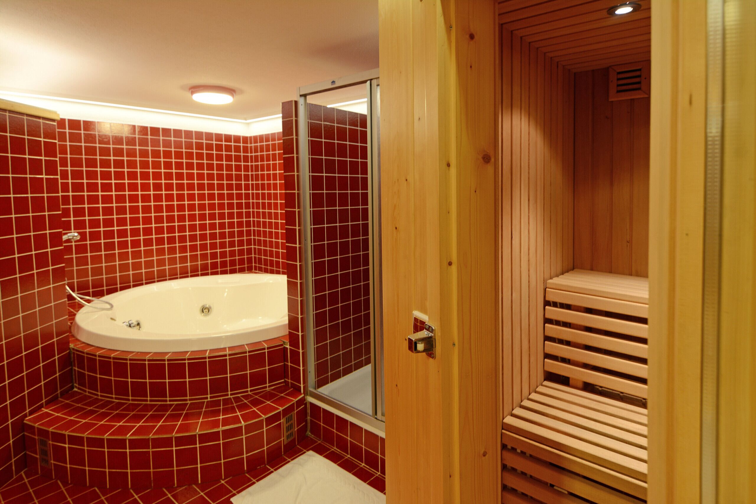Une salle de bain avec un sauna en bois, une douche en verre et une baignoire recouverte de carreaux rouges.