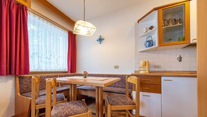 A cozy kitchen with wooden furniture, a dining table, and a window with red curtains. - Apartments Jasmin 101C (Selva di Val Gardena)