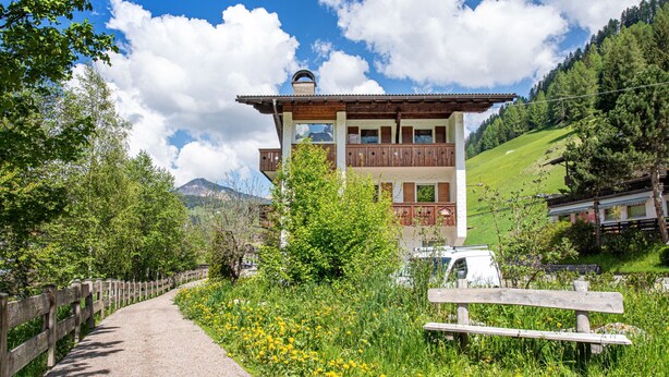 A traditional chalet with a wooden balcony, surrounded by lush greenery and a clear sky. - Apartments Jasmin 101C (Selva di Val Gardena)