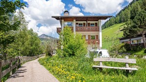 En traditionel chalet med en træbalkon, omgivet af frodig vegetation og en klar himmel.