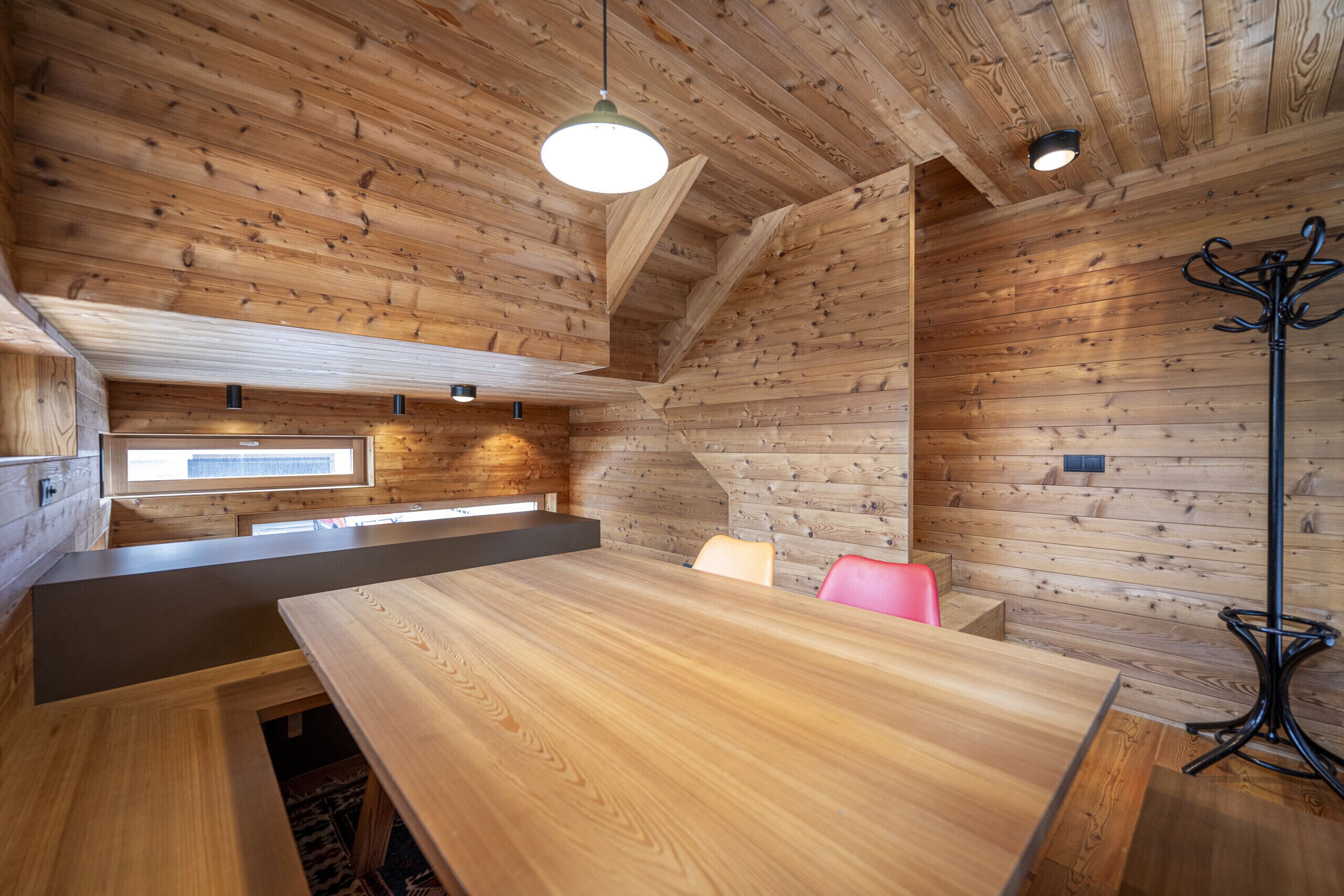 Un interior de madera con una larga mesa, sillas, un banco y un perchero.