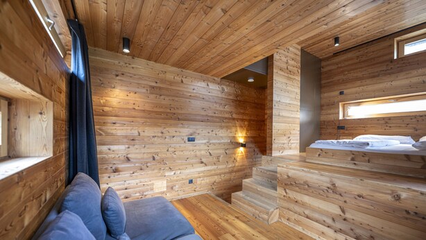 Interior de uma cabana de madeira com uma cama, um sofá e uma escada.