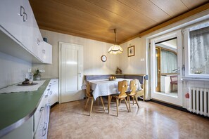 A kitchen with wooden cabinets, a dining table with chairs, a hanging light fixture, and a window with curtains.