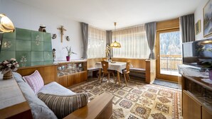 Ein gemütliches Wohnzimmer mit Sofa, Esstisch und Stühlen, einem grünen Schrank und einem Fenster mit Vorhängen.