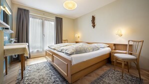 Ein Schlafzimmer mit einem Bett, einem Schreibtisch, einem Stuhl, einem Spiegel und einem Fenster mit Vorhängen.
