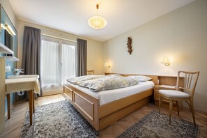 A bedroom with a bed, a desk, a chair, a mirror, and a window with curtains.