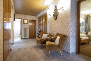 A hotel room with a wooden ceiling, a patterned wall, a sofa, a small table, and a bookshelf. - 137A Apartments Raieta (Ortisei)