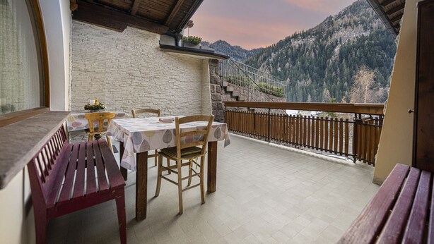 Ein Balkon mit Tisch und Stühlen, einer hölzernen Bank und Blick auf eine gebirgige Landschaft.