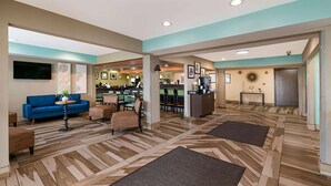 A spacious lobby with a blue sofa, a wooden floor, and a reception desk. - Baymont by Wyndham Elizabeth City (Elizabeth City)