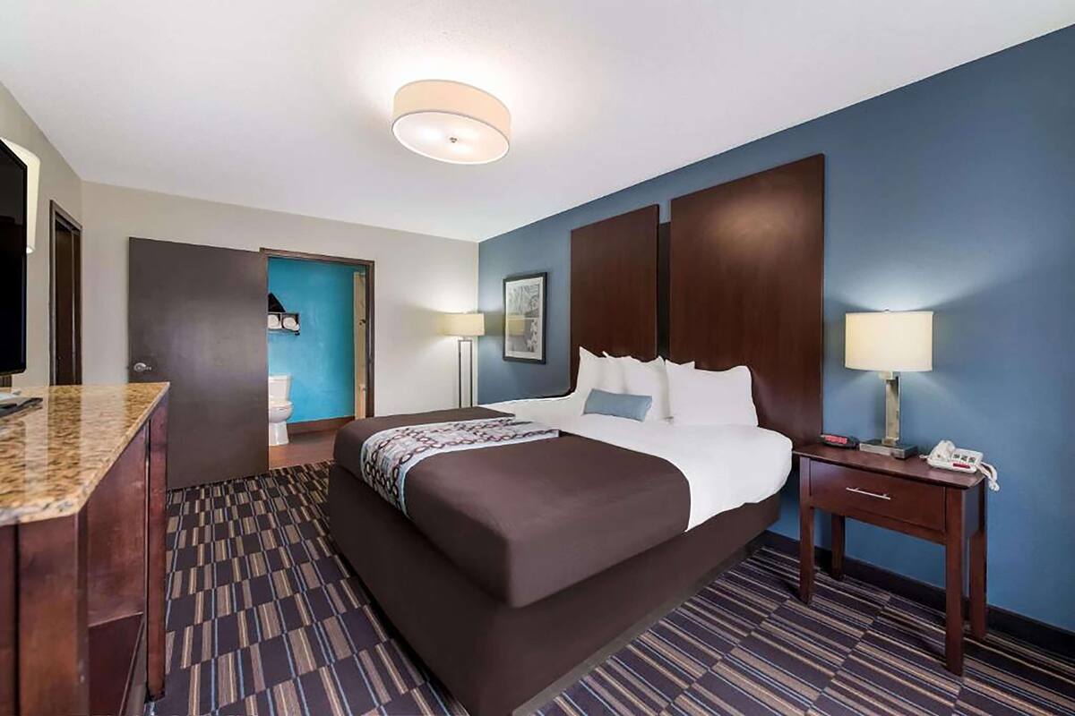 Ein Hotelzimmer mit einem großen Bett, einem Schreibtisch, einem Sessel, einem Nachttisch, einer Lampe und einem Telefon.