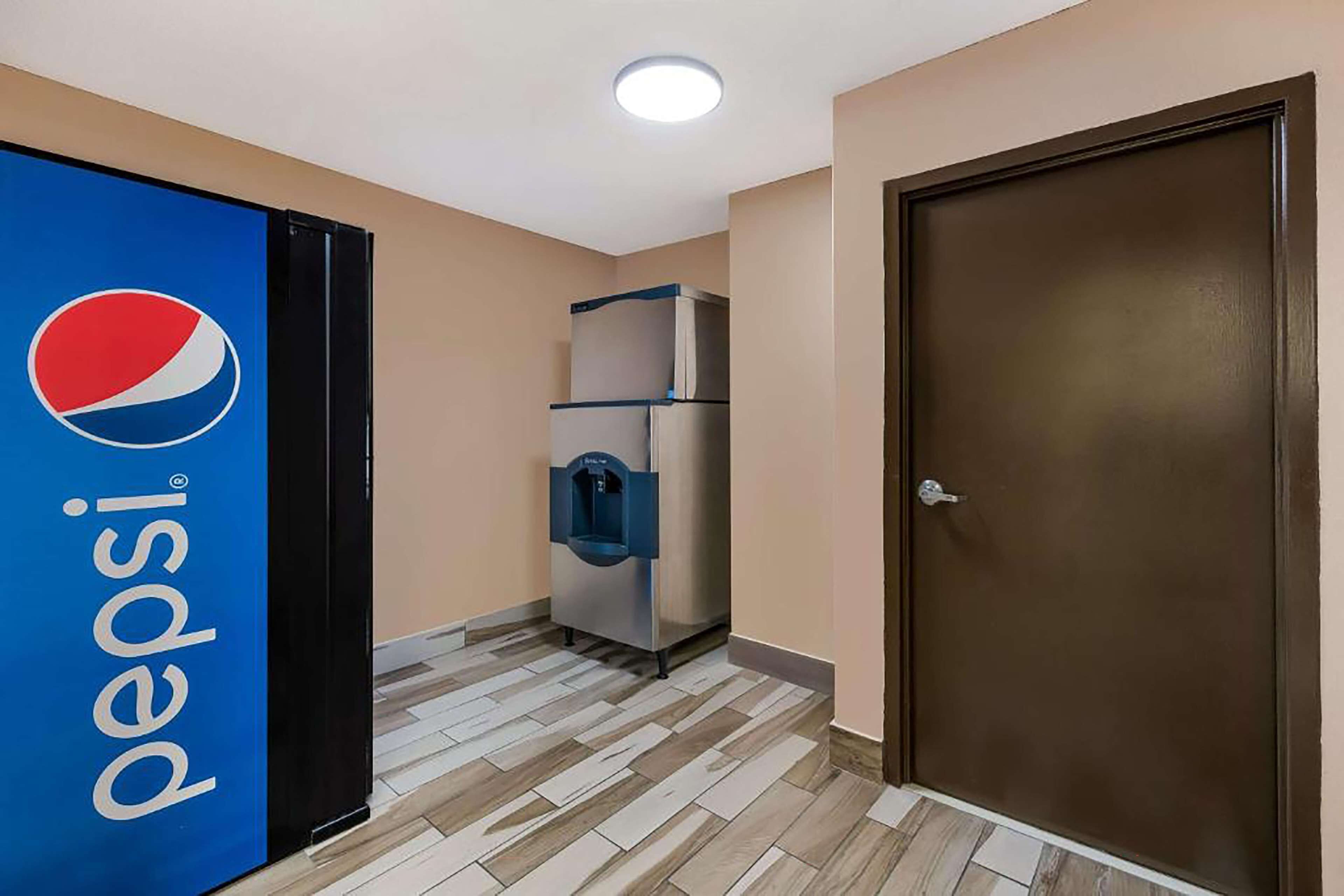 A hallway with a Pepsi refrigerator, a water dispenser, and a brown door.