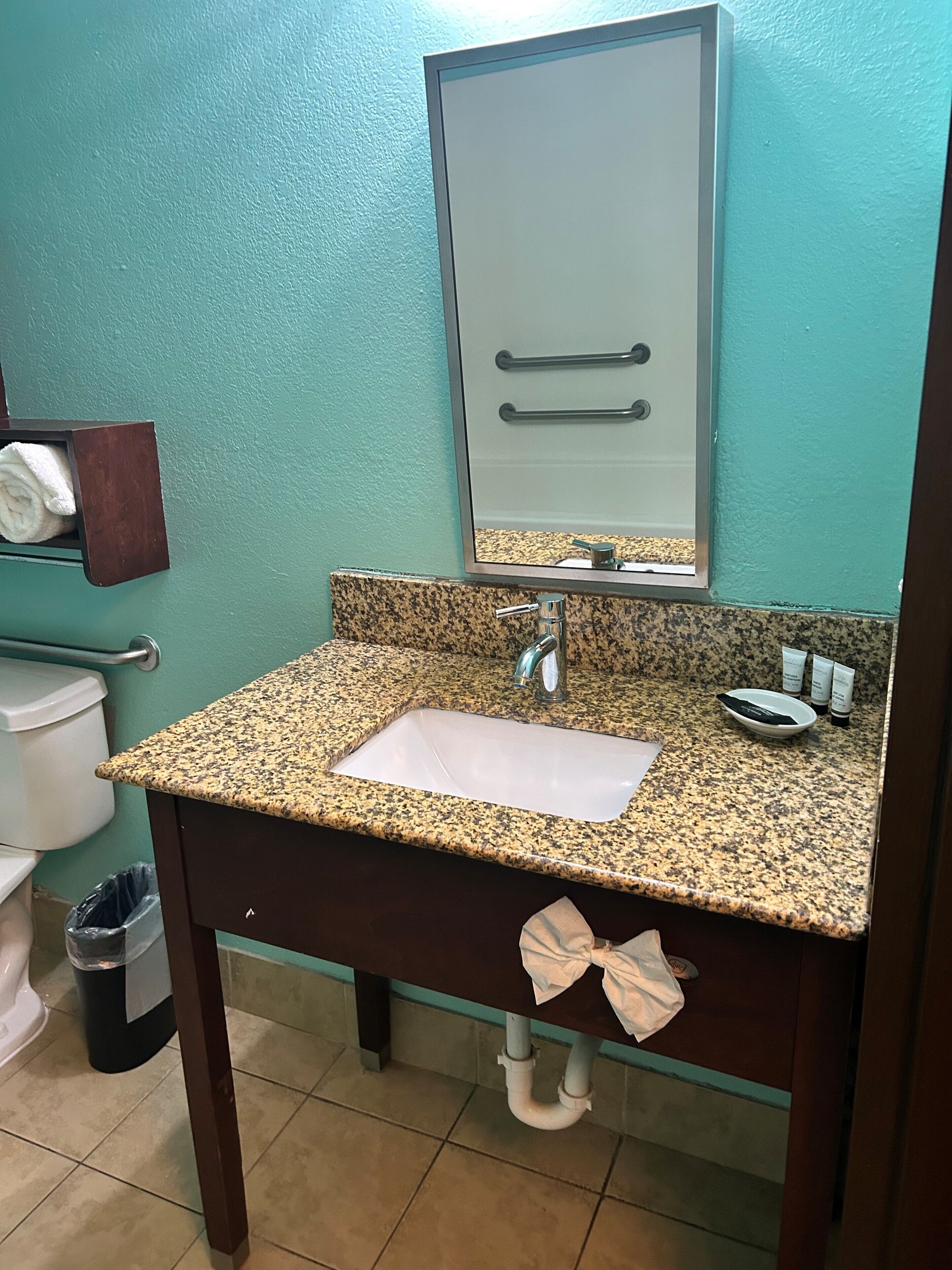 A bathroom with a granite countertop sink, a mirror, and a towel rack.
