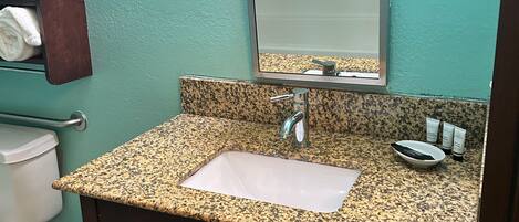 A bathroom with a granite countertop sink, a mirror, and a towel rack.