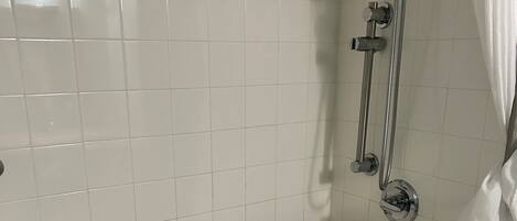 A bathroom with white tiled walls, a bathtub with a grab bar, and a shower with a handheld showerhead.
