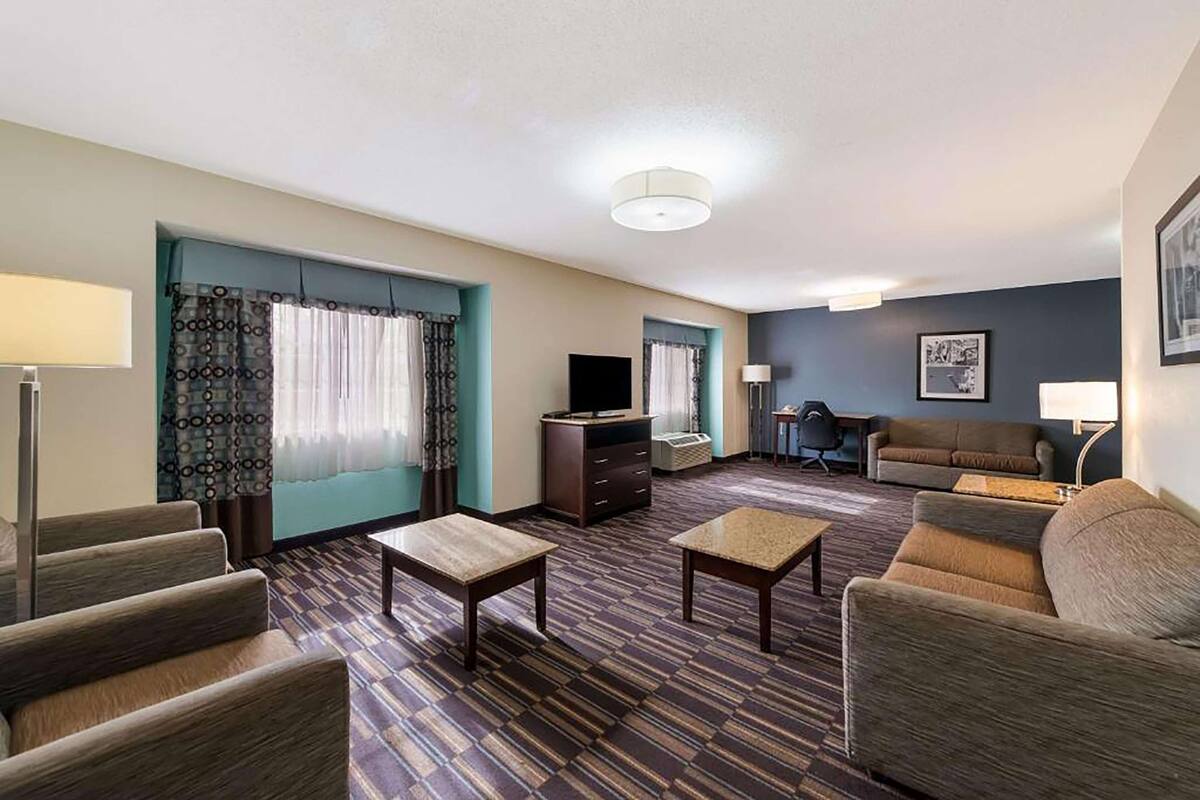 Ein Hotelzimmer mit einer Couch, zwei Sesseln, einem Couchtisch, einem Fernseher, einem Schreibtisch und einer Lampe.